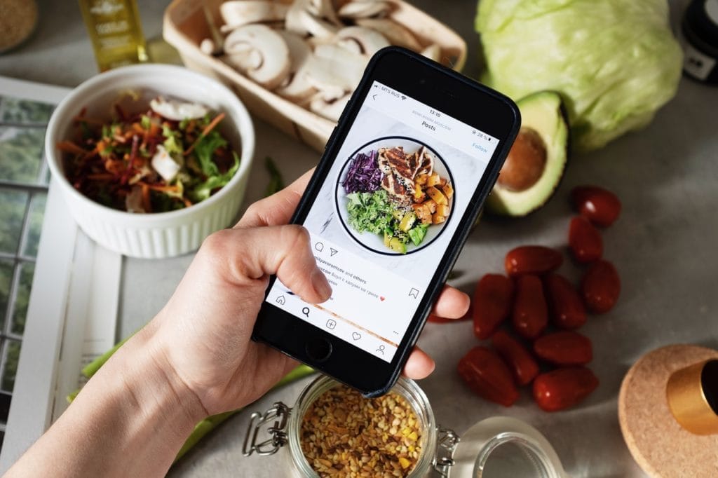 Una mano sujeta un teléfono que muestra la foto de un plato de ensalada en Instagram